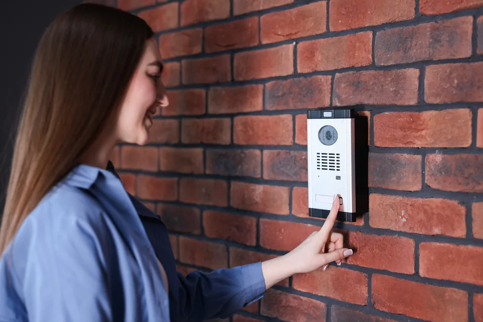 Woman pressing a video intercom button on a brick wall